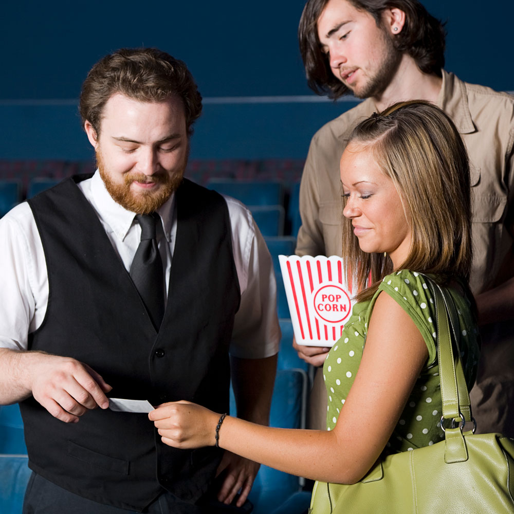 A young man and woman showing a movie ticket to an employee to get help finding their seats